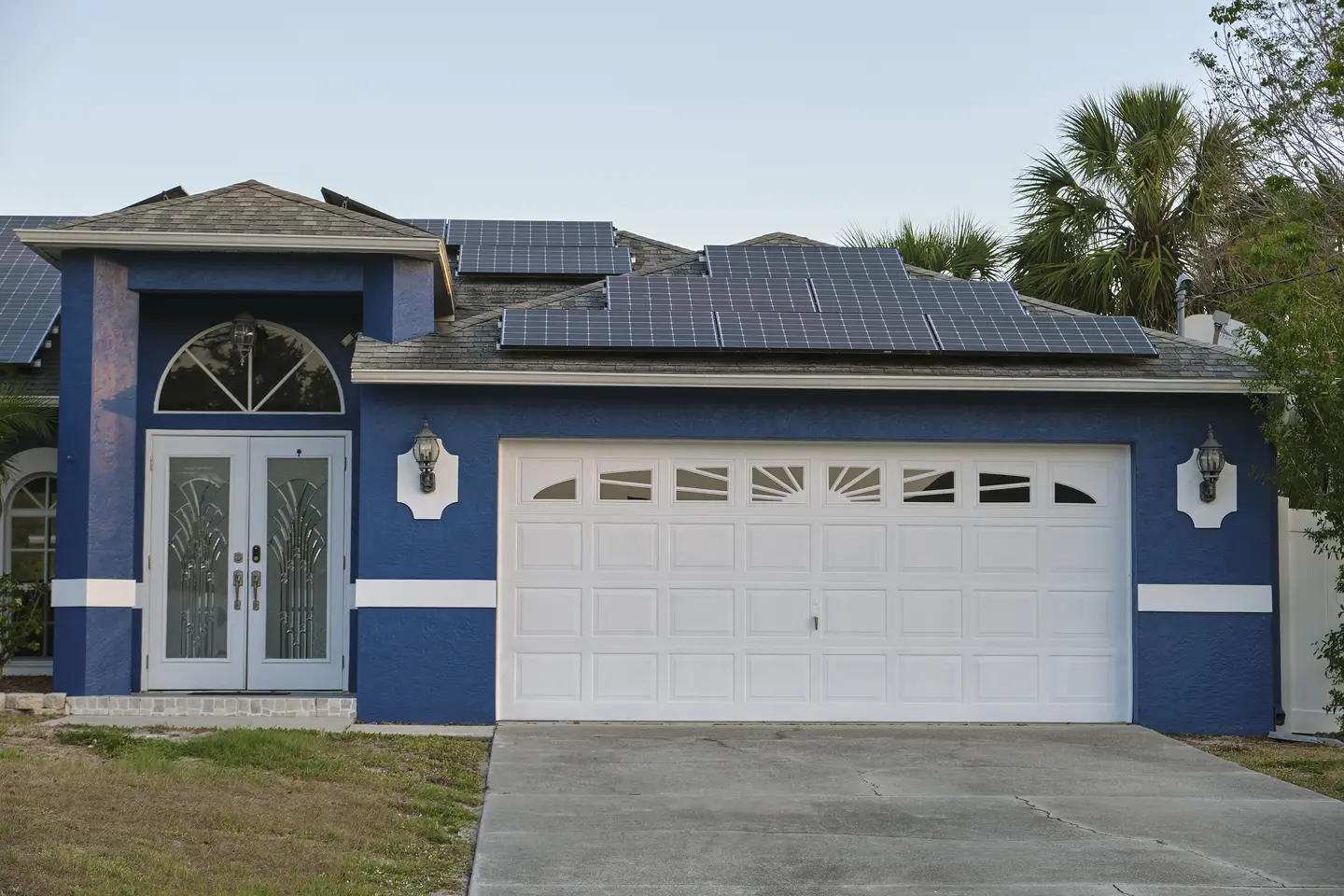 A blue and white home with solar panels on the roof, a double-car garage, and a glass and wood front door