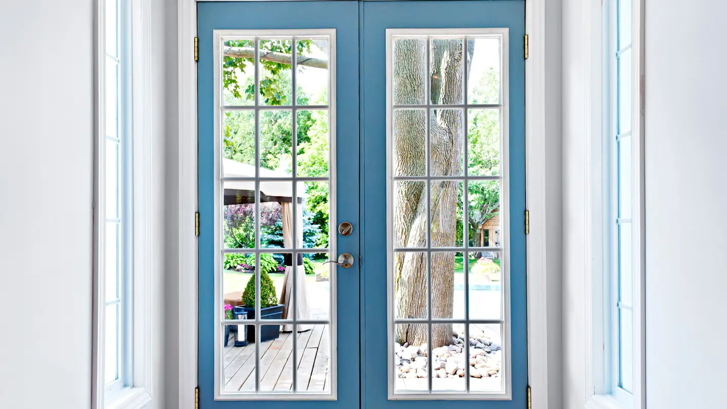 Blue patio door looking out to a yard with a deck and tree.